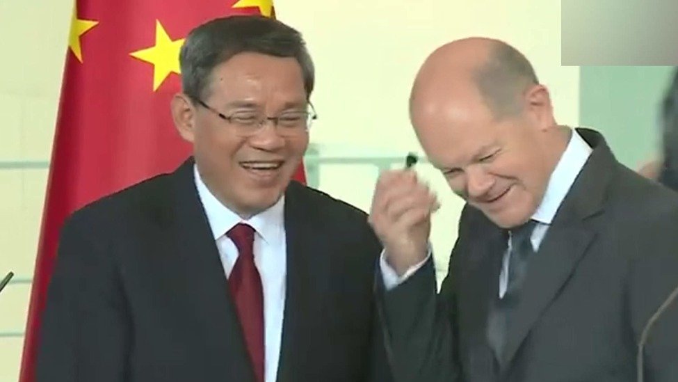 中德两国总理与双方人员合影前，李强提醒朔尔茨摘耳机