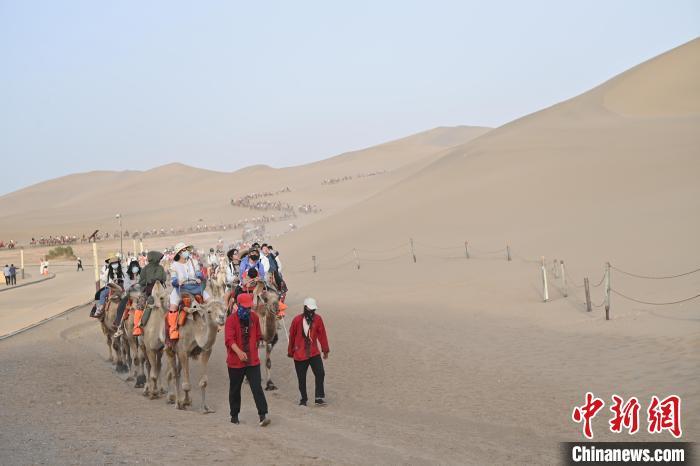 游客骑乘骆驼在鸣沙山月牙泉景区游览。 九美旦增 摄