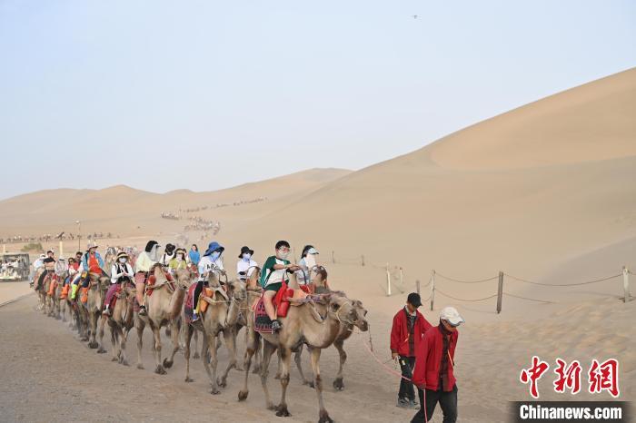 图为游客骑乘骆驼在鸣沙山月牙泉景区游览。 九美旦增 摄