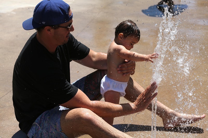 △当地时间7月3日，美国亚哥拉山，一名男子带孩子在公园的喷泉玩水降温。