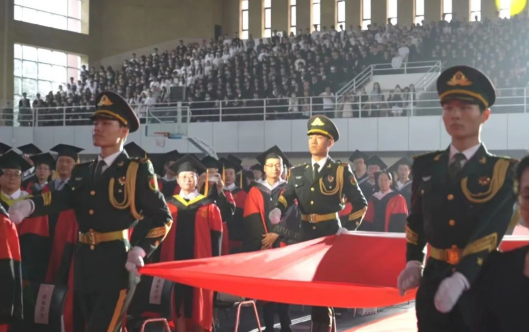 国旗护卫队旗手迈着矫健的步伐护送国旗入场。师生肃立，向国旗行注目礼。