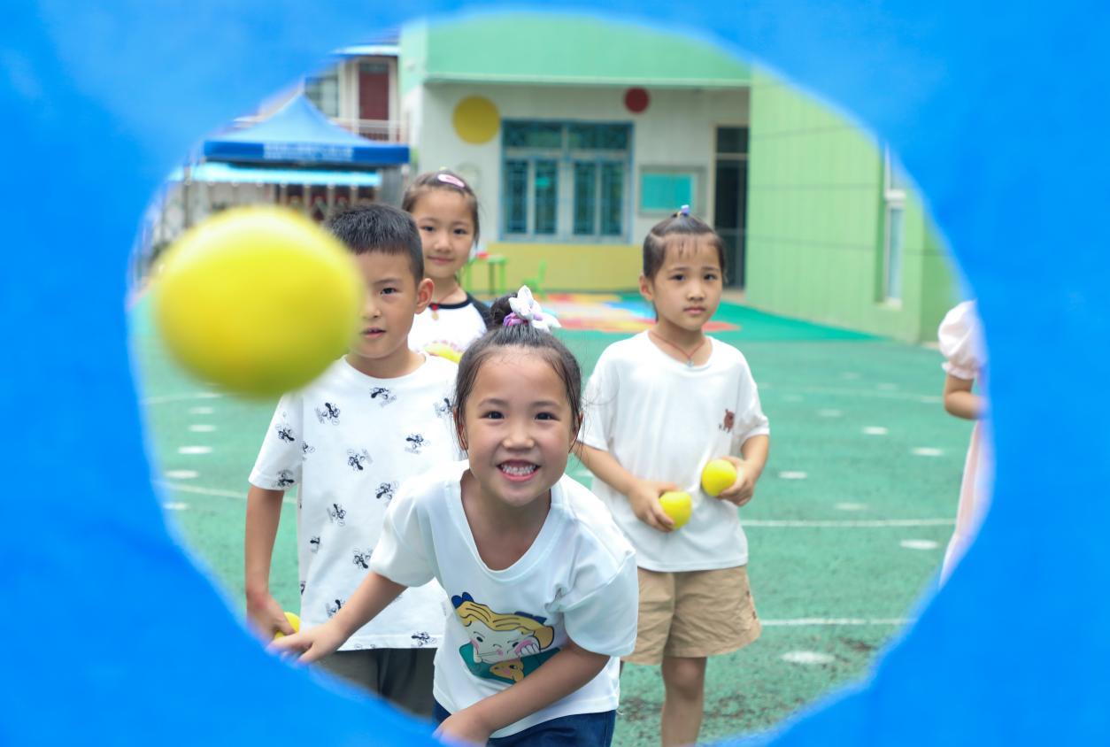 （2023年7月13日，在安徽省合肥市肥西县山南镇中心幼儿园，孩子们在玩布洞投球游戏。 陈家乐 摄）
