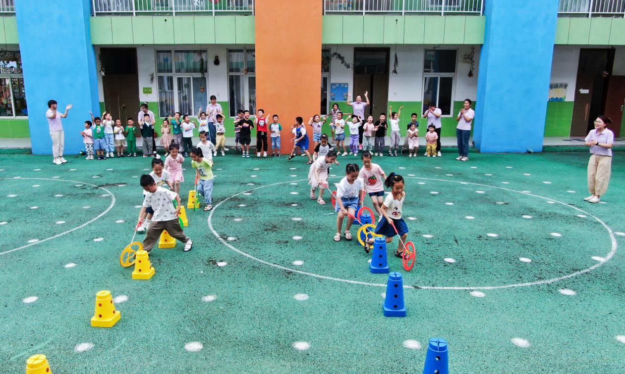 （2023年7月13日，在安徽省合肥市肥西县山南镇中心幼儿园，孩子们在玩滚铁环游戏。（无人机照片） 陈家乐 摄）