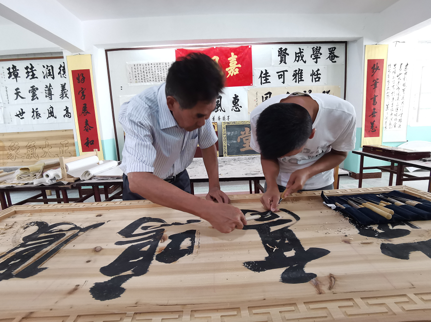 赣南客家匾额习俗的传承人肖天长(左)指导徒弟肖伟明(右)制作匾额。（李梦丽 摄）