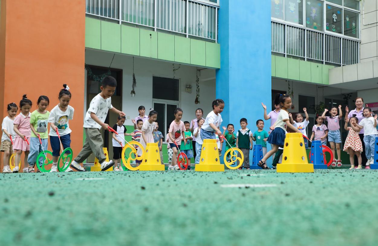 （2023年7月13日，在安徽省合肥市肥西县山南镇中心幼儿园，孩子们在玩滚铁环游戏。 陈家乐 摄）
