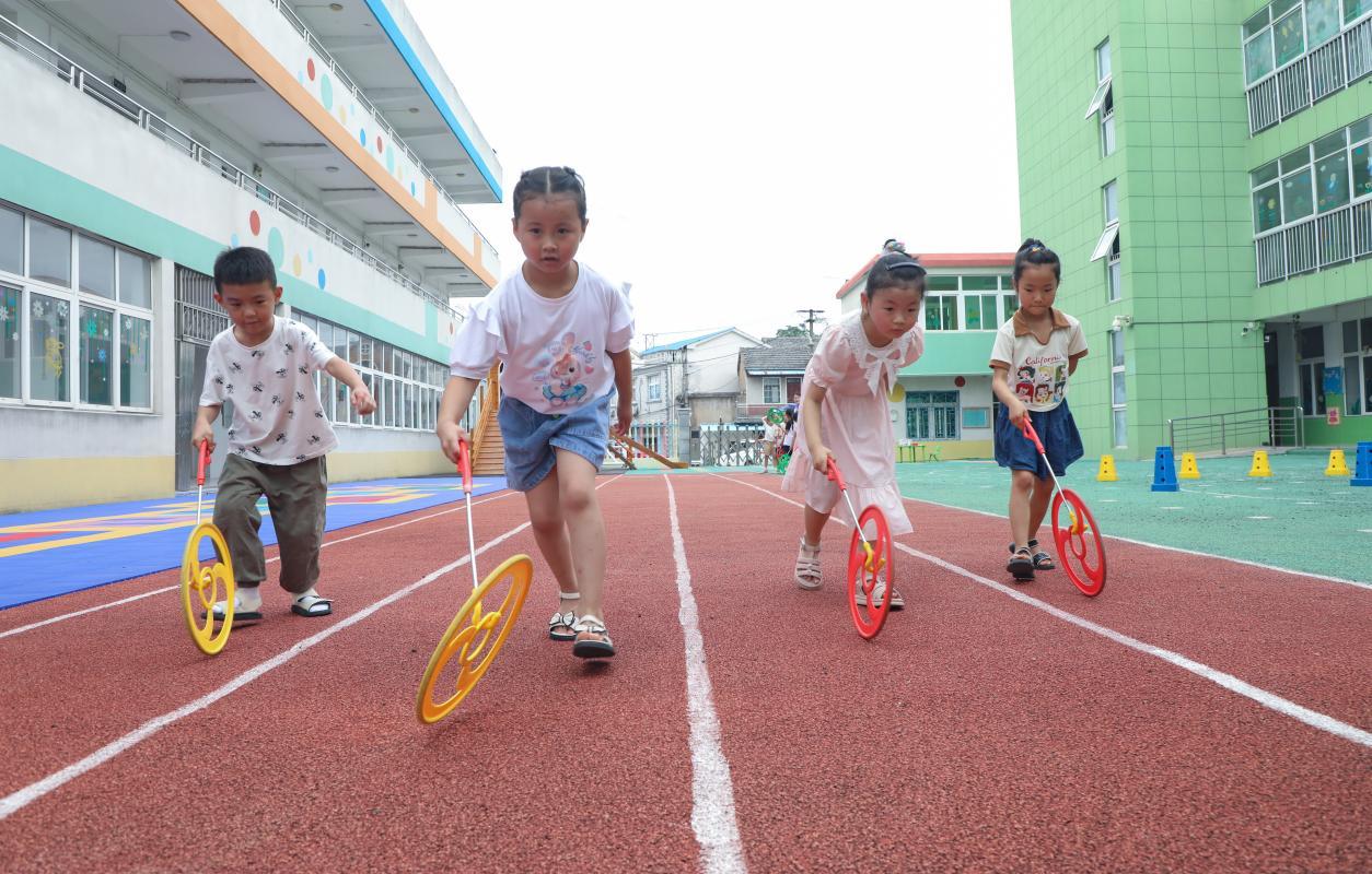 （2023年7月13日，在安徽省合肥市肥西县山南镇中心幼儿园，孩子们在玩滚铁环游戏。 陈家乐 摄）