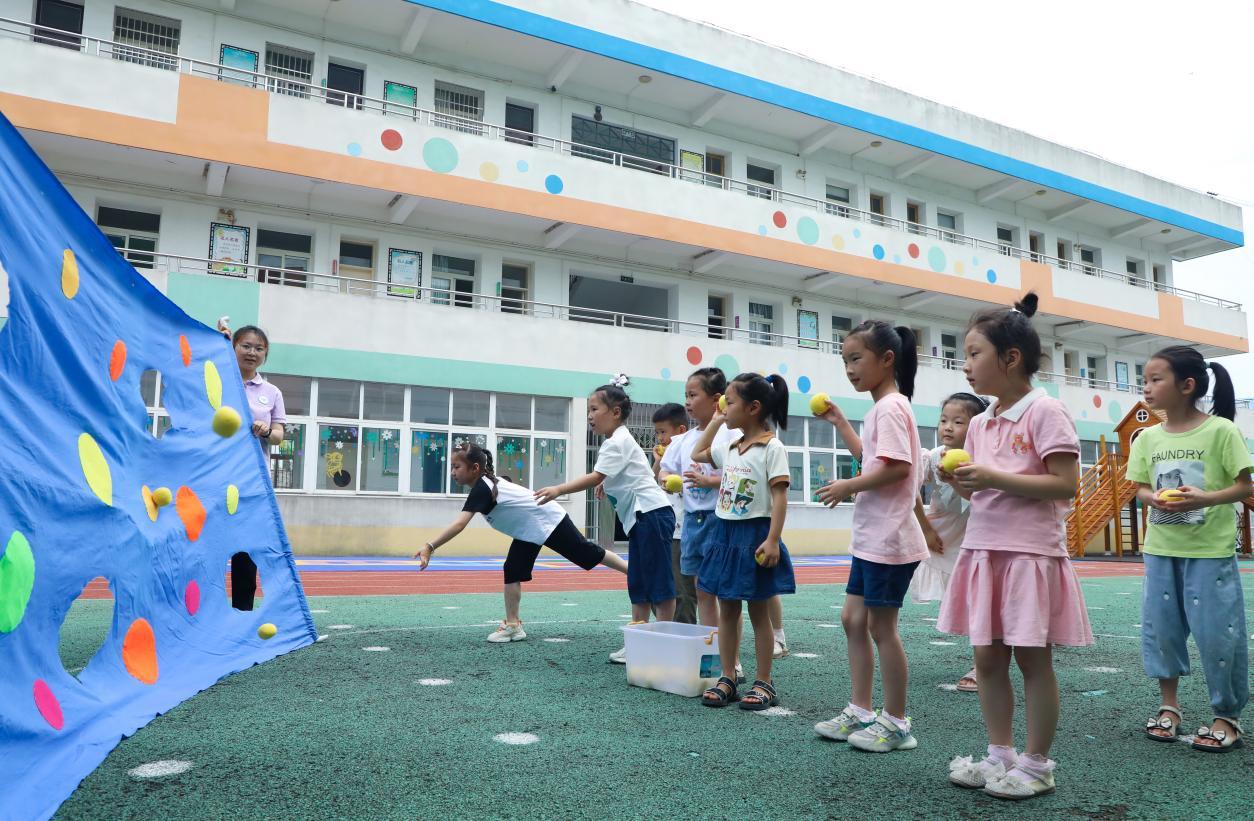（2023年7月13日，在安徽省合肥市肥西县山南镇中心幼儿园，孩子们在玩布洞投球游戏。 陈家乐 摄）