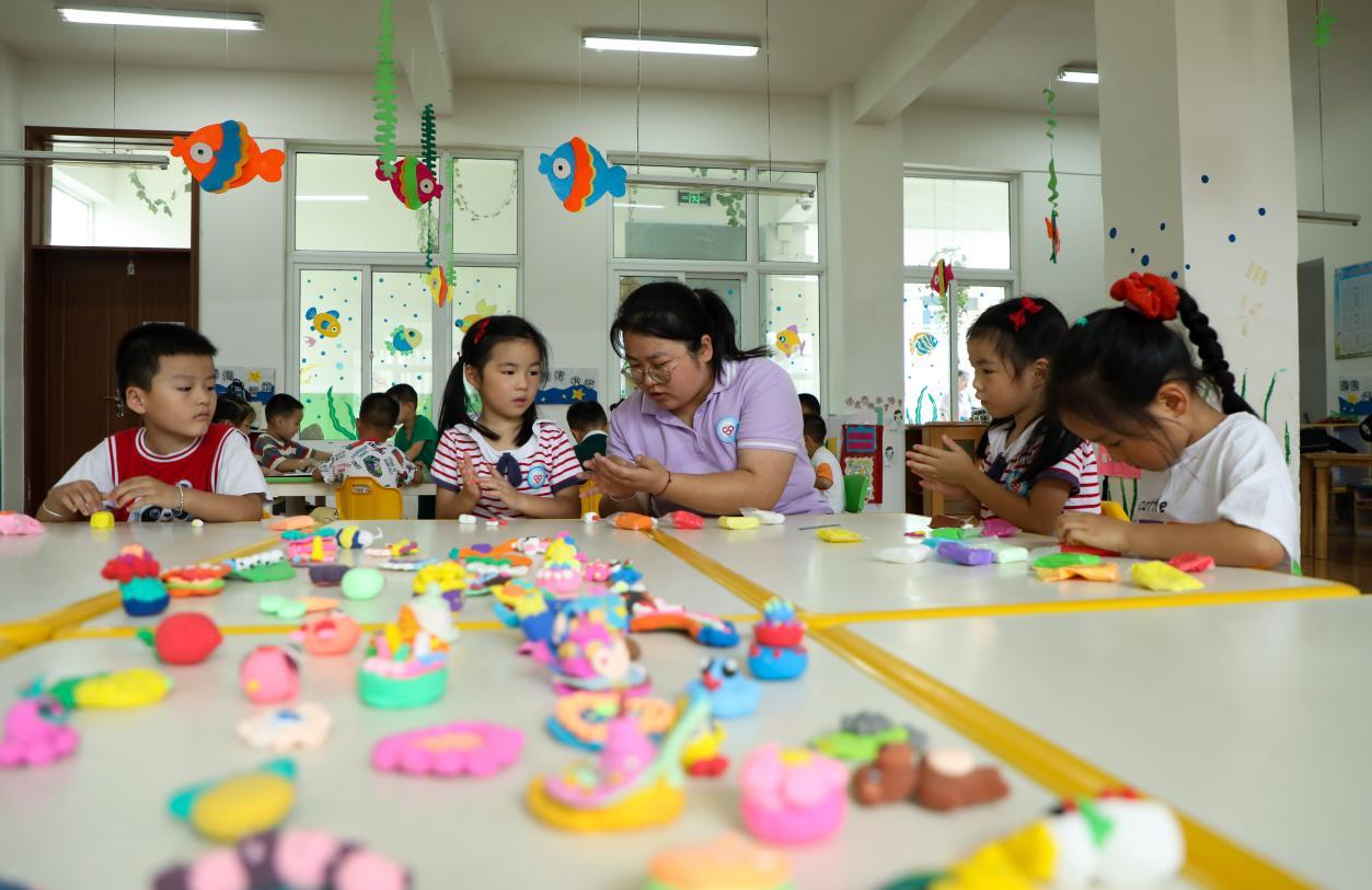 （2023年7月13日，在安徽省合肥市肥西县山南镇中心幼儿园，孩子们在老师的指导下做彩色泥塑。 陈家乐 摄）