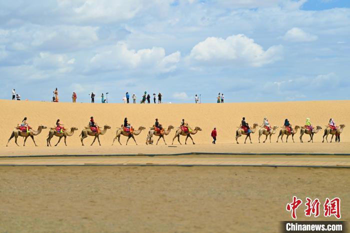 7月21日，甘肃敦煌鸣沙山月牙泉景区内，游客在驼队旁进行旅拍。中新社记者 李亚龙 摄