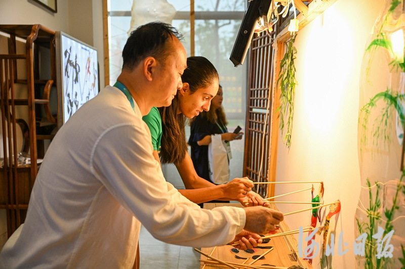 8月1日，成都皮影艺术博物馆馆长赵洪（左）在指导巴西运动员操作皮影。
