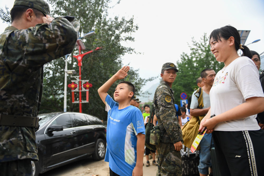 8月2日，在北京市门头沟区妙峰山镇，在乘坐车辆转移前，来自内蒙古的三年级小学生武天骐（中）向武警北京总队机动第三支队的王雷鸣敬礼感谢。新华社记者 鞠焕宗 摄