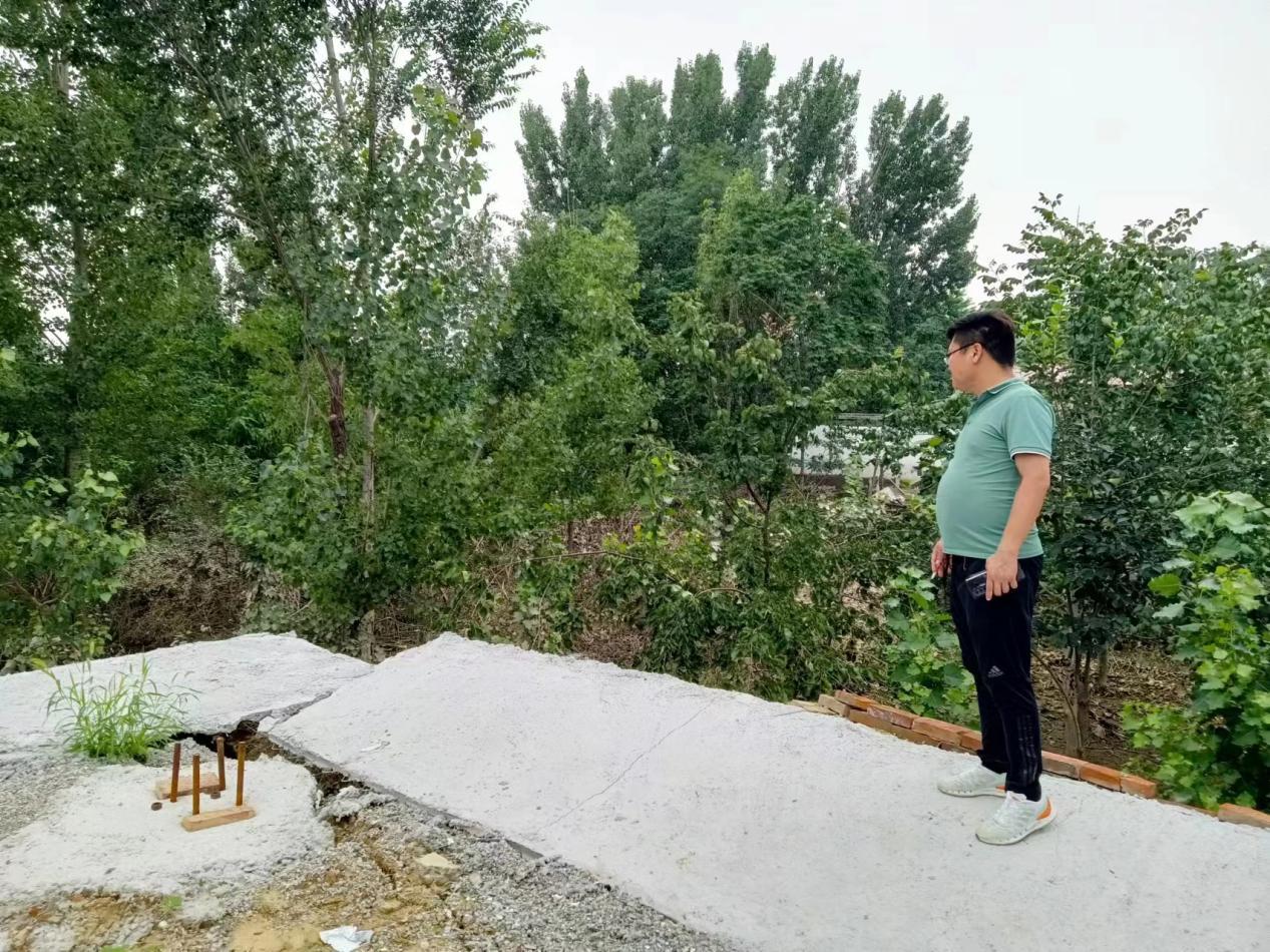 刘金涛站在暴雨冲毁的车棚地基上