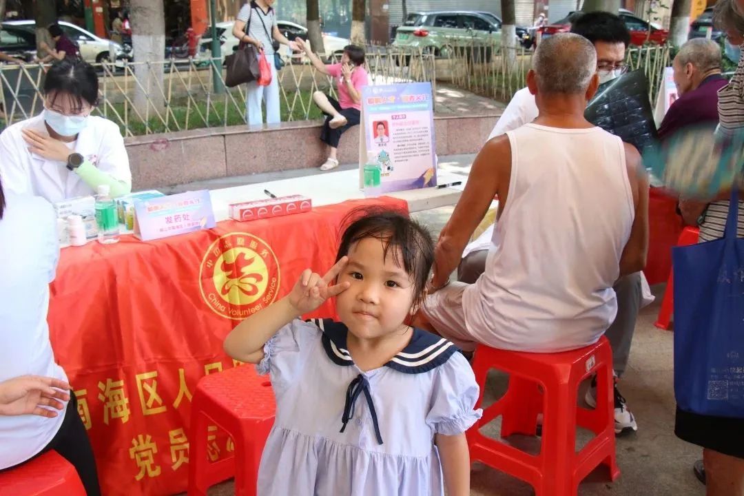 人群中的医务人员与义诊摊位前等待家人就诊的小女孩