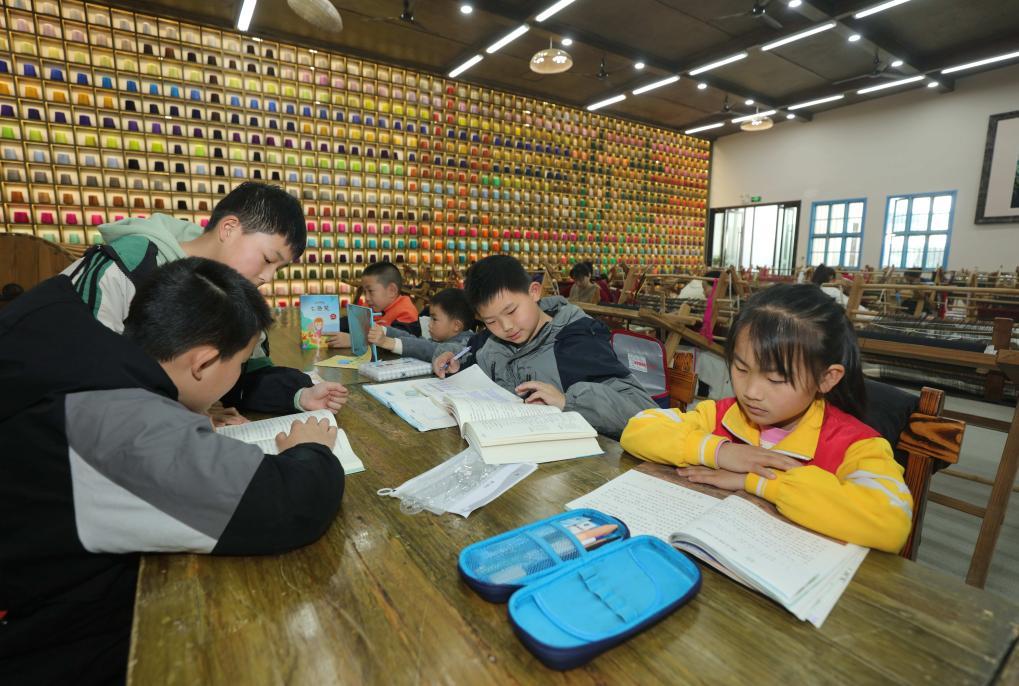 “媽媽工廠”里，媽媽們忙著織錦，孩子們則在一旁學(xué)習(xí)。（吳勇兵 攝）