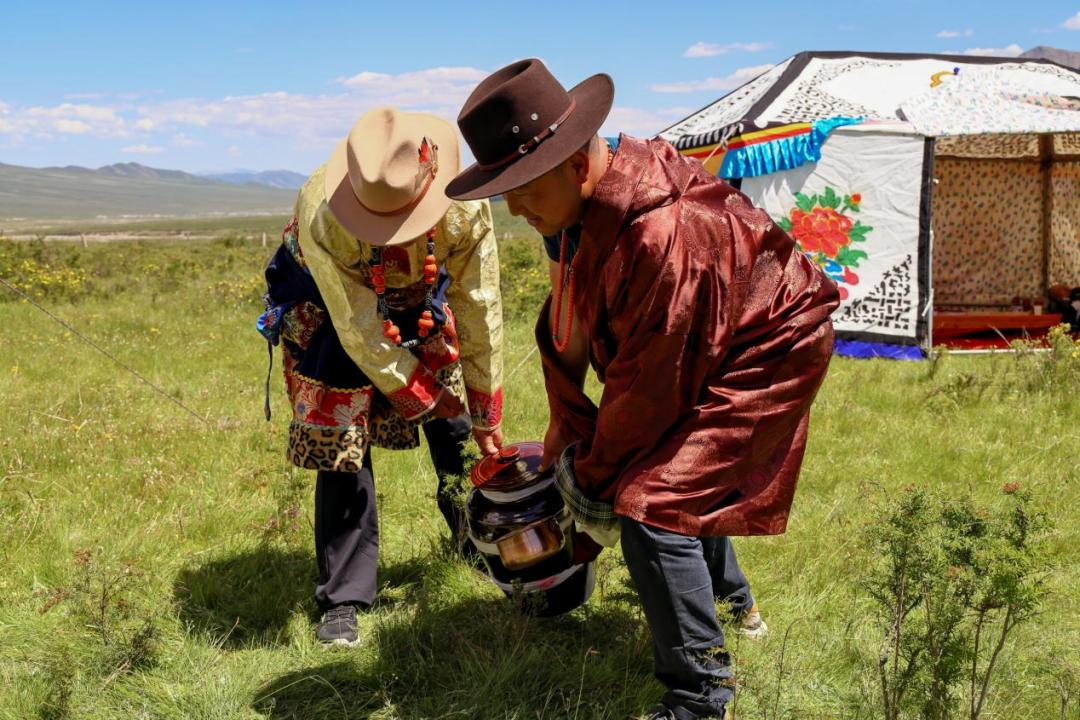 “羌钦”(抬大酒)仪式,两名男子扮做吃力的模样吆喝着将酒坛抬到帐篷内。