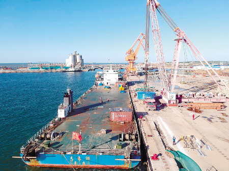 500吨桅杆式起重机将166吨的风电电机吊装到货船甲板上。