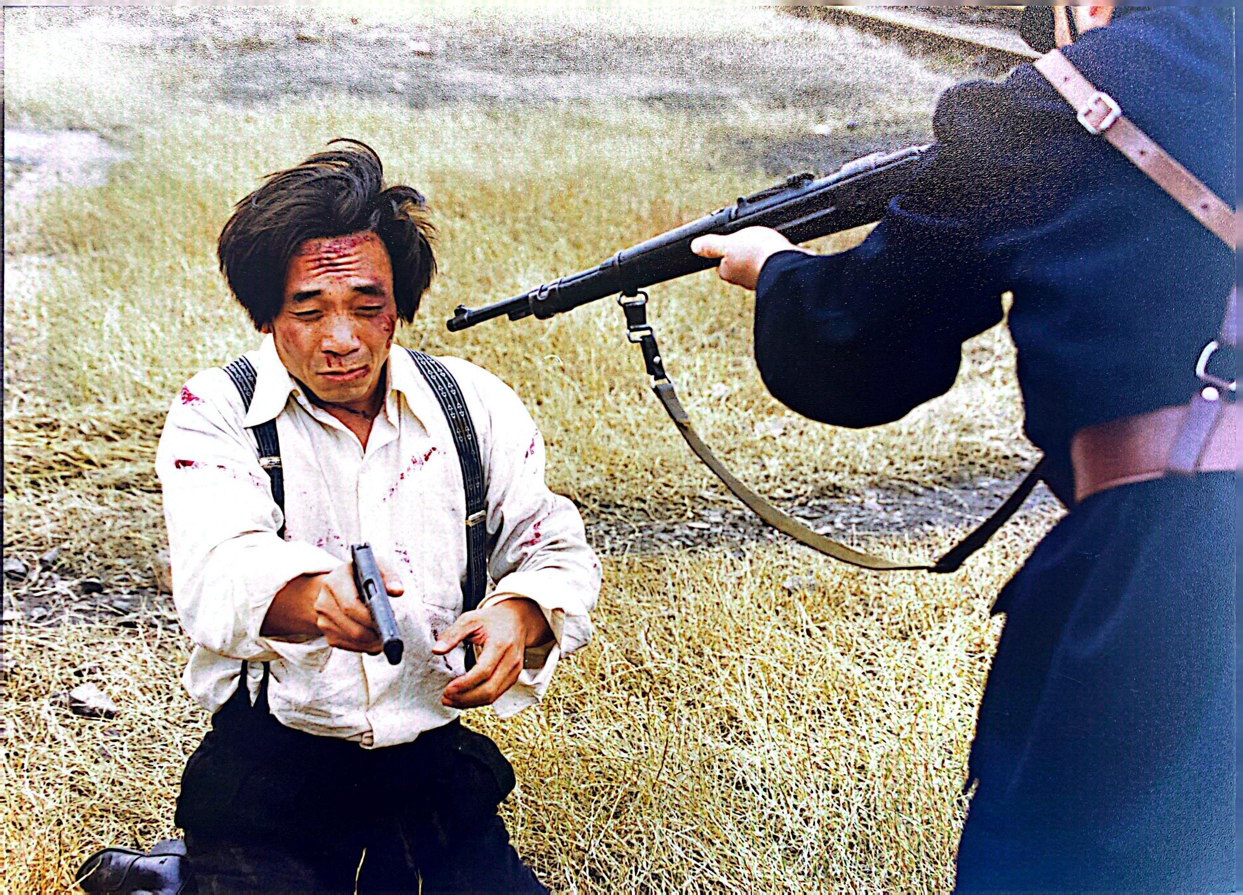 叛徒皓明在敌人的威逼下，把枪口对准了自己的同志。