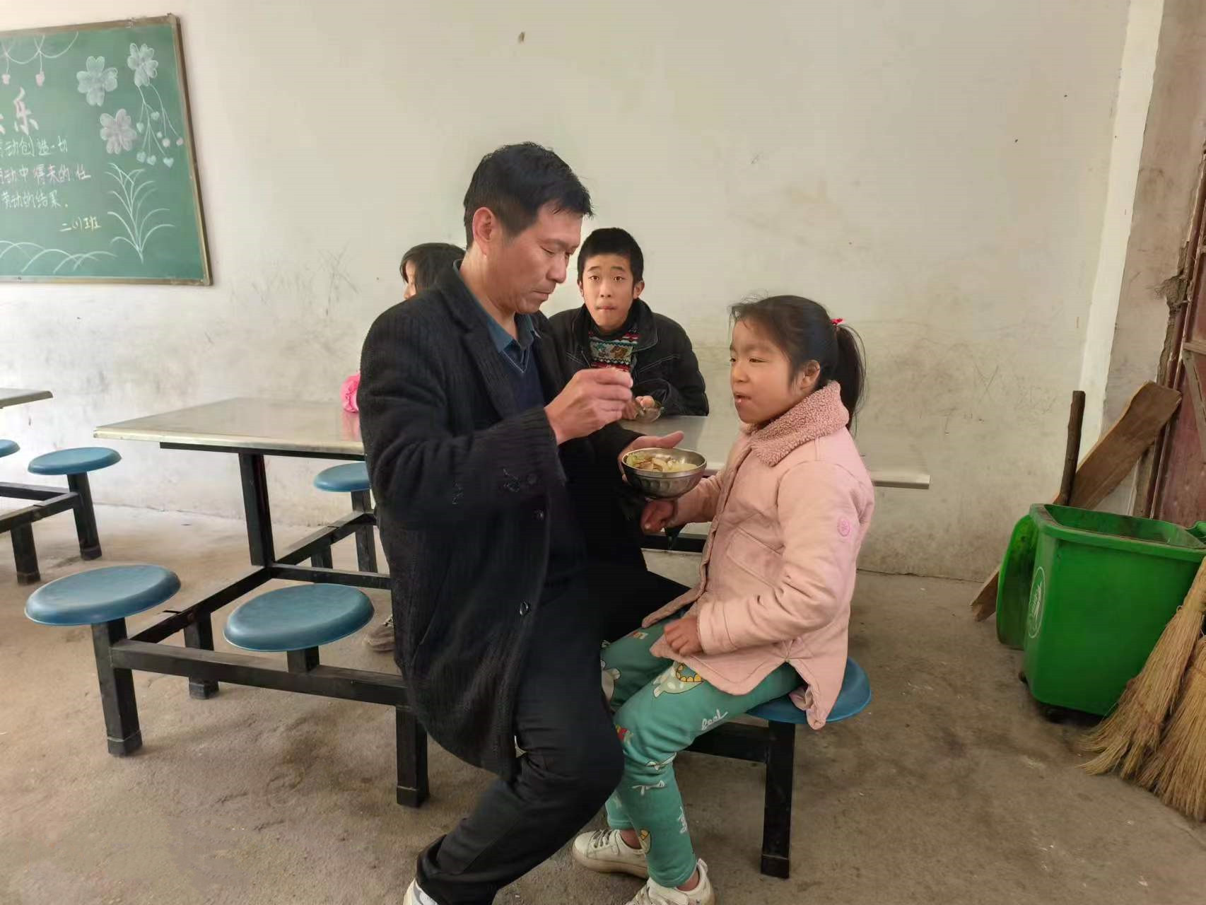 石龙伟在学校餐厅给学生喂饭。