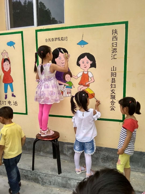 孩子们在某村广场的墙上绘制“反校园霸凌”主题的墙画。