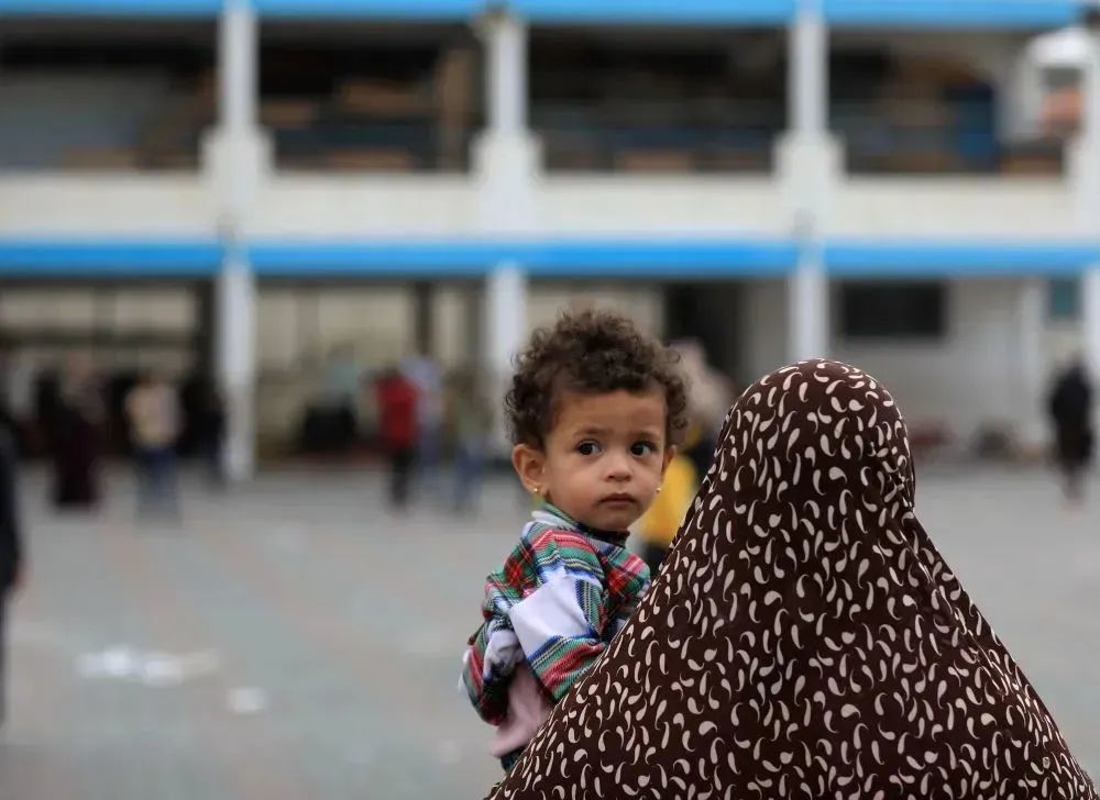 10月9日，一名妇女抱着小孩在加沙地带南部城市汗尤尼斯的一所学校躲避以色列空袭 图：新华社