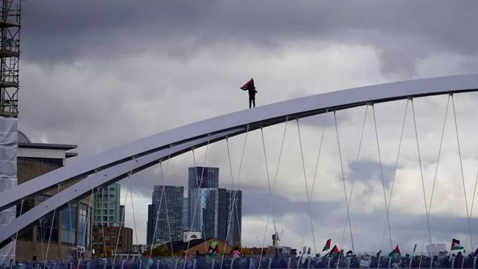 英国数千人举行游行抗议BBC对加沙事件的报道，一名抗议者爬上索尔福德码头大桥，挥舞巴勒斯坦国旗