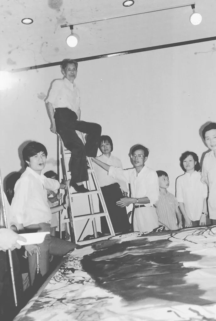 1985年深圳美术节笔会现场，吴冠中爬上梯子观看画作效果。