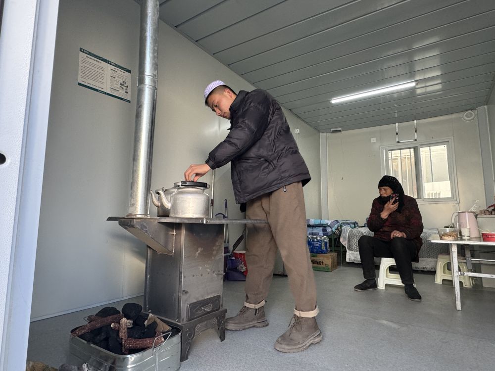 2023年12月30日，在甘肃省临夏州积石山县大河家镇大河村安置点的板房内，马文英（左一）在查看火炉。新华社记者　任延昕　摄
