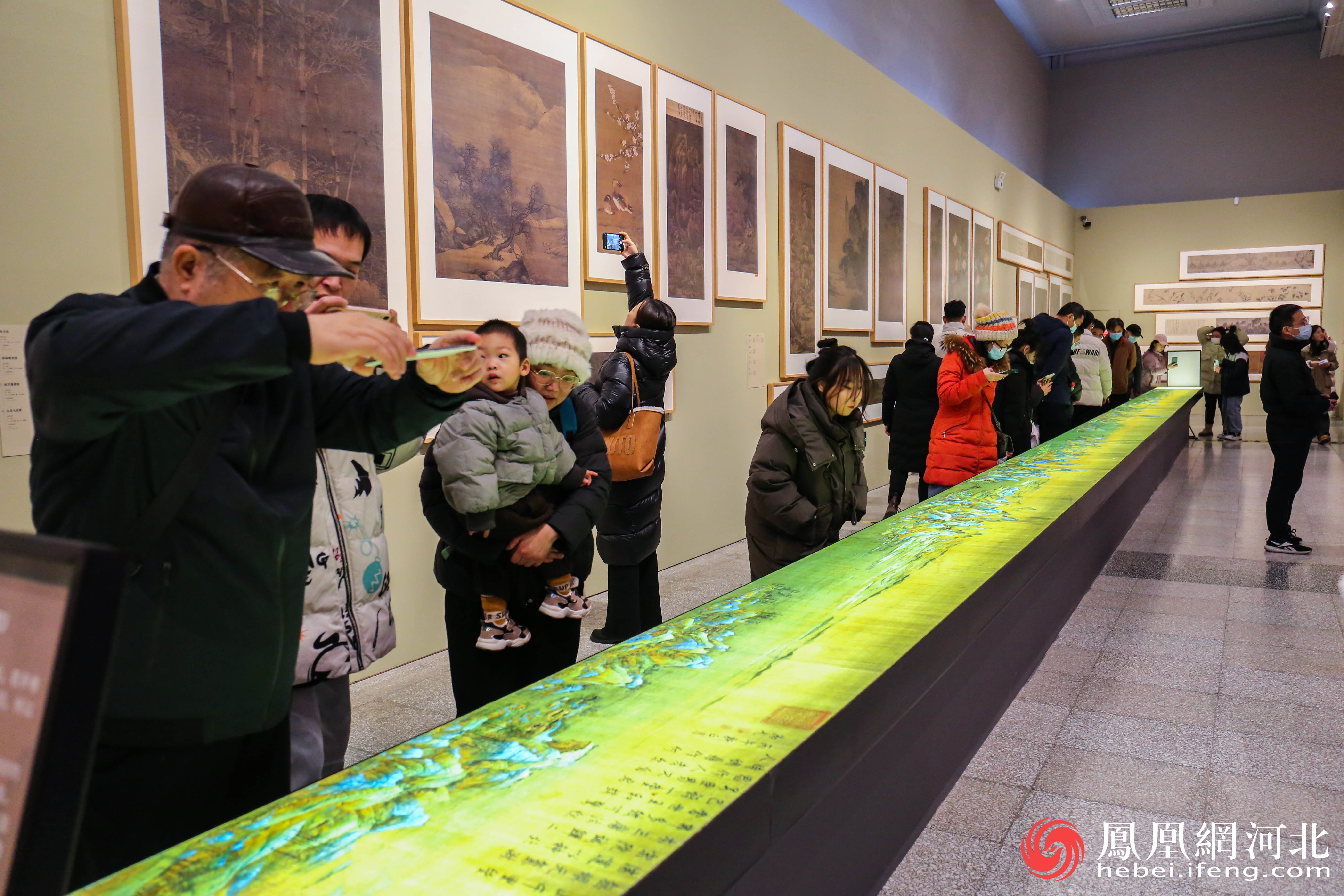 《千里江山图》围满了观众弯腰凑近观看画作细节，拍照欣赏。