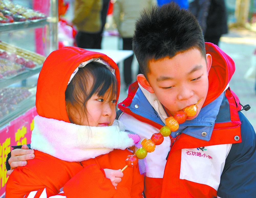 兄妹俩在分享香甜的冰糖葫芦，感受传统小吃的味道。