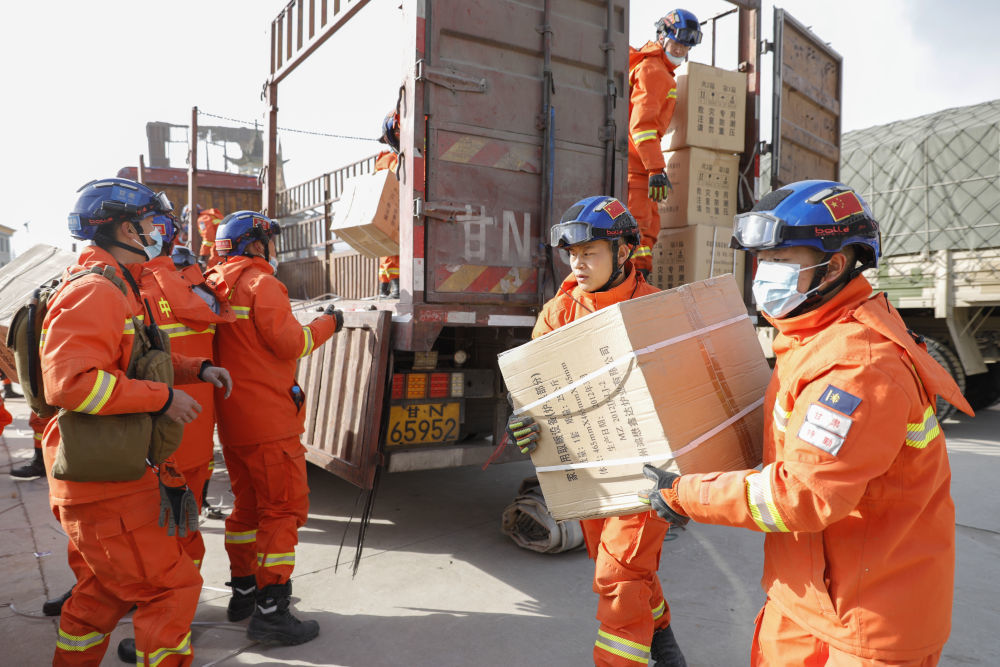 2023年12月19日，在甘肃临夏积石山县大河家镇大河村安置点，消防人员在搬运救援物资。
