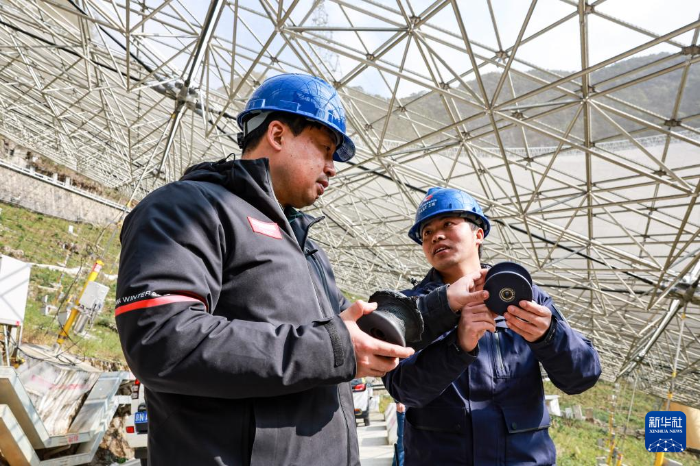姜鹏（左）在贵州“中国天眼”的反射面板下与工作人员交谈（2023年2月13日维护保养期间拍摄）。新华社记者 欧东衢 摄
