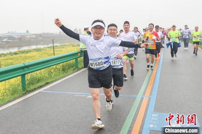 图为选手们开心地奔跑在金色油菜花旁的鄱阳湖堤坝公路上。刘力鑫摄