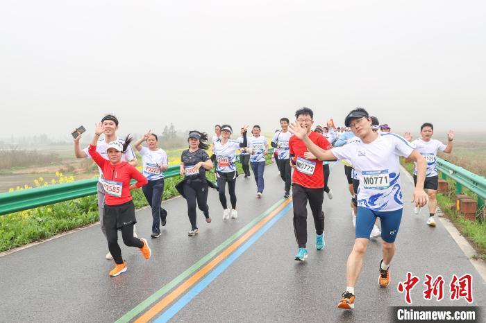 图为选手们开心地奔跑在金色油菜花旁的鄱阳湖堤坝公路上。刘力鑫摄