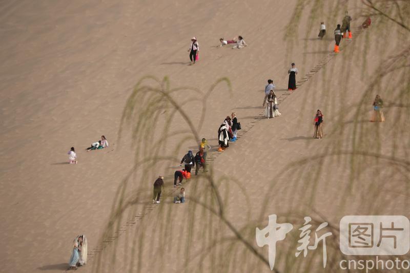 2024年3月24日,游客在甘肃省敦煌市鸣沙山月牙泉景区游览。中新社发 张晓亮 摄