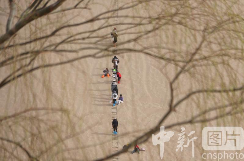 2024年3月24日,游客在甘肃省敦煌市鸣沙山月牙泉景区游览。中新社发 张晓亮 摄