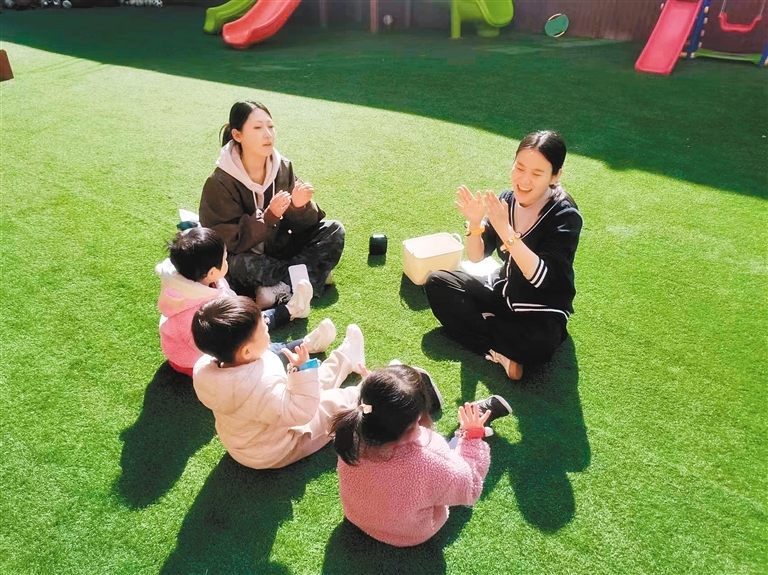 漳浒寨街道文兴巷社区托育园的保育师带着小朋友在户外上音乐课