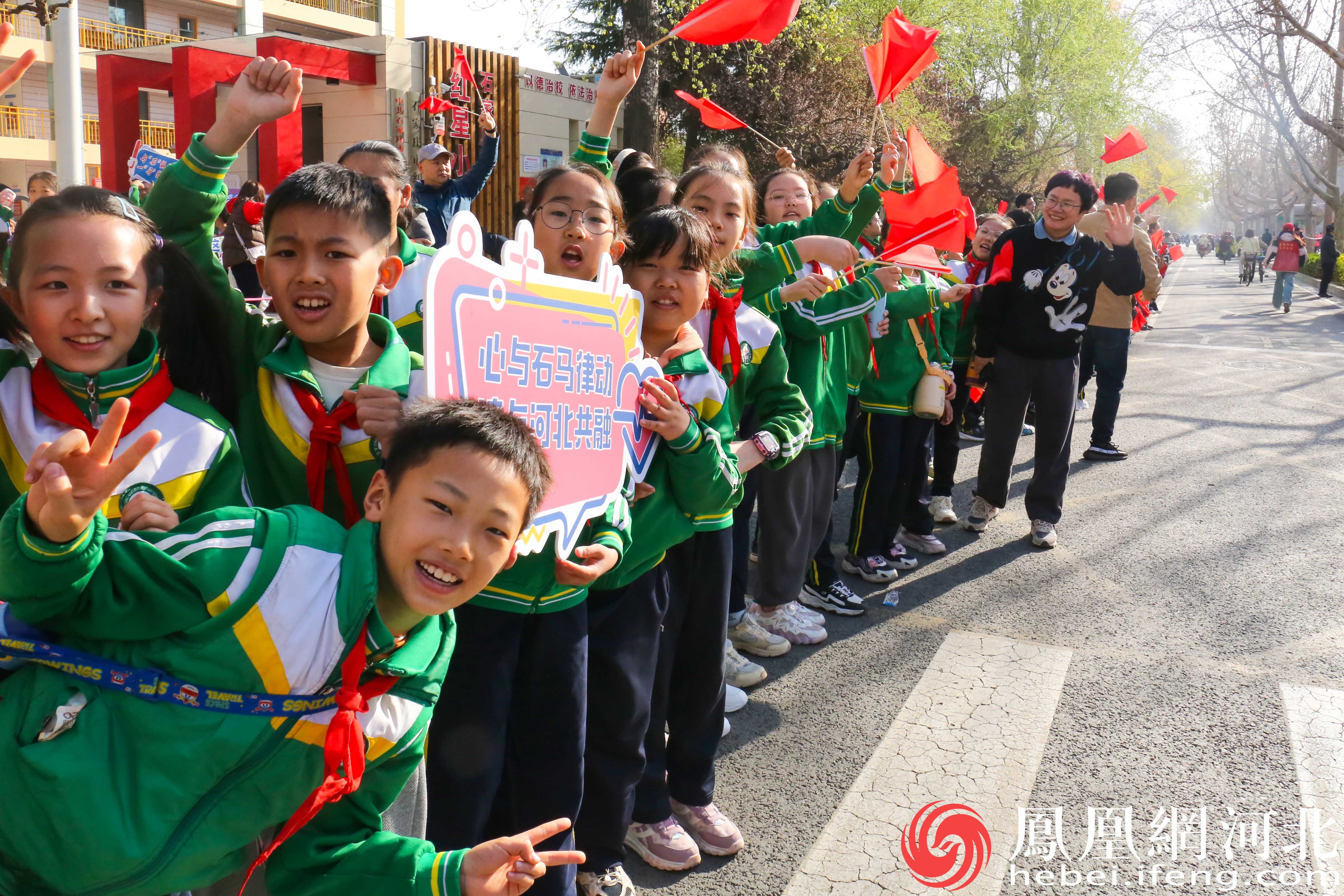 小学生们自发地聚集在赛道旁，为参赛选手们加油助威。他们穿着整齐的校服，手持小旗子和标语，脸上洋溢着兴奋和期待的笑容。
