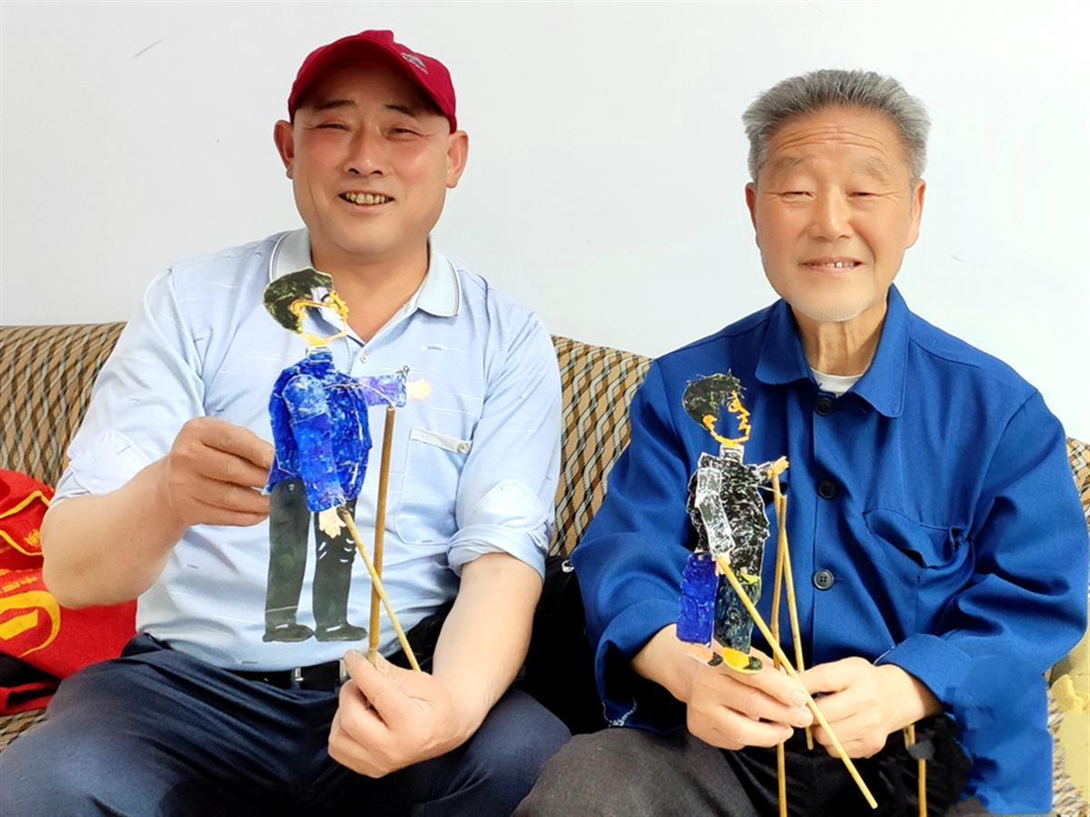 图为陈中祥（右）正在和周承志展示新雕刻的皮影道具.png