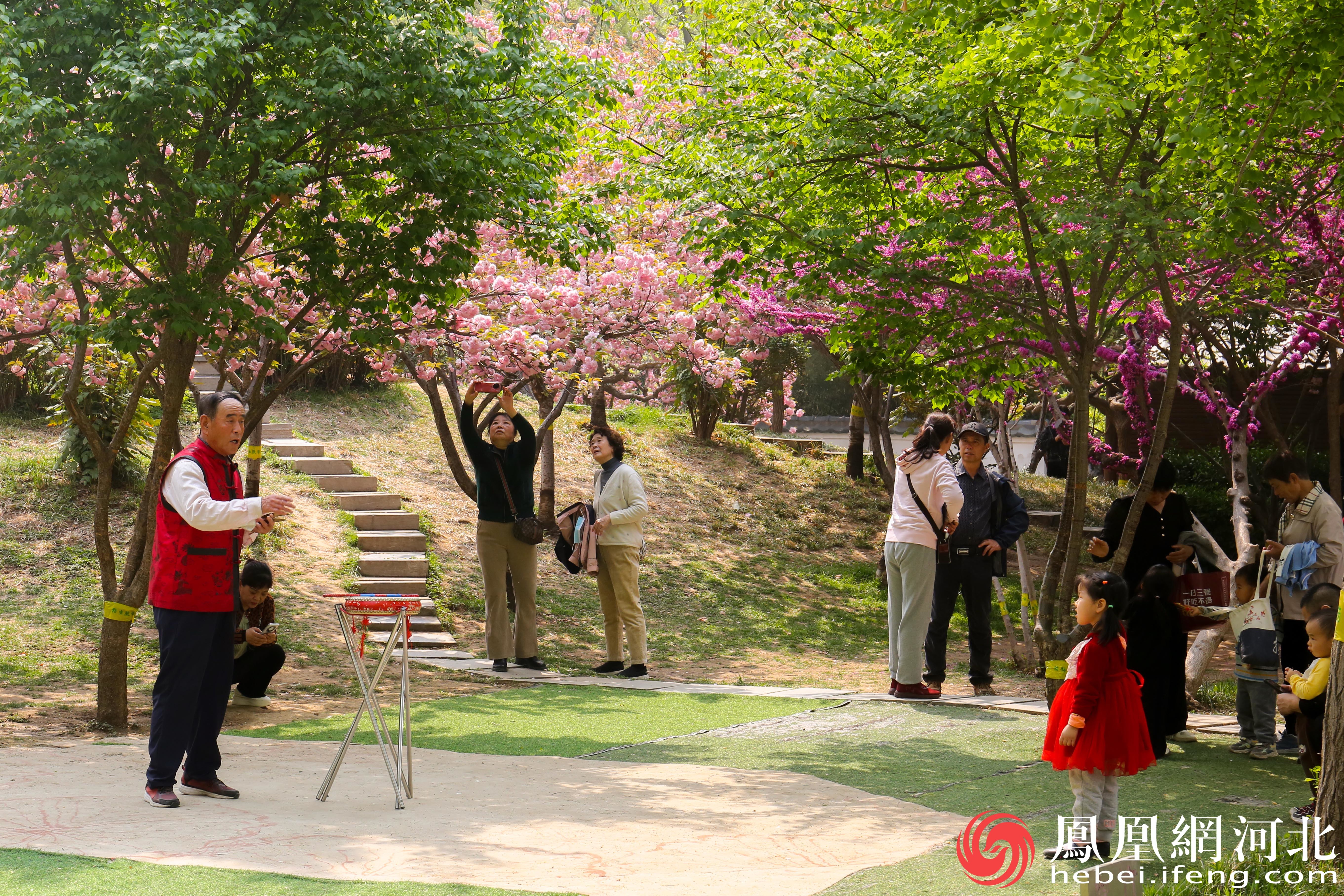 在石门公园的一角老人、女孩和盛开的花朵都融为一体，共同构成了一个充满诗意和温馨的场景。