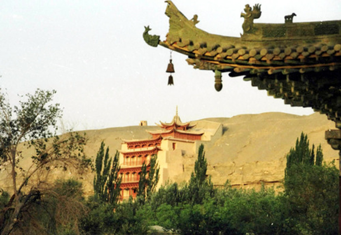 从20世纪70年代末开始，大量先进科技不断被引入敦煌石窟保护。新技术、新材料、新手段的不断运用，丰富了敦煌遗产的保护技术和保护手段，有效改变了石窟内部及其环境的保护状况，使敦煌遗产的保护工作从原来的抢救性保护，过渡到了科学保护阶段。图为透过敦煌莫高窟前的牌楼一角望去，敦煌莫高窟标志性建筑九层楼依旧雄伟壮观。新华社记者　梁强　摄（2004年10月25日发）