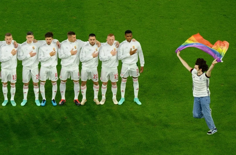 一名球迷挥舞着彩虹旗在匈牙利球员面前奔跑。