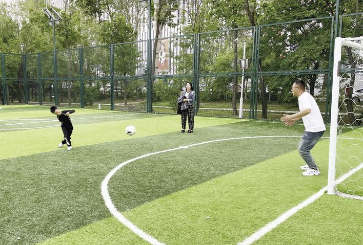 街边的运动场地里,一家人其乐融融感受足球的快乐。