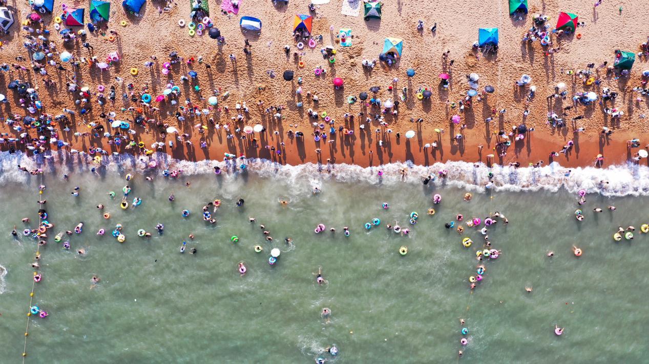 人们纷纷跃入海中，带着五颜六色的游泳圈趣味十足。丁敏航 摄