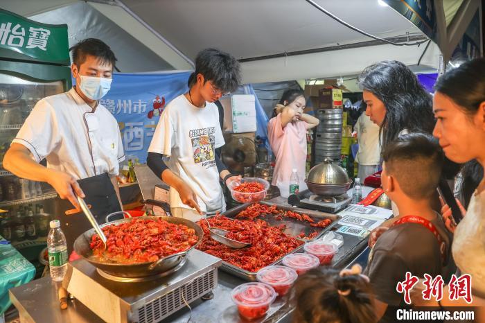 7月25日，江西赣州南康区，2024赣州市龙虾啤酒节在南康家居小镇开幕，众多民众来到现场逛夜市品美食，享受夏日夜晚的人间烟火气。图为民众在购买小龙虾。中新社记者 刘力鑫 摄