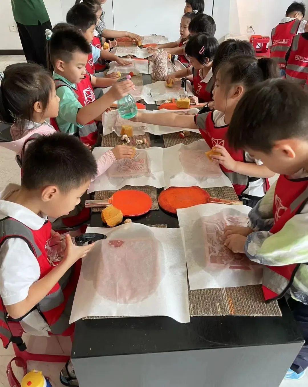 孩子们将宣纸覆在范版上,海绵按压后拓包蘸朱砂上色,使图案映在宣纸上。图源 / 陕西汉唐石刻博物馆