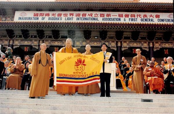 国际佛光会世界总会成立暨第一届会员代表大会在西来寺举行，大师与慈容法师向大众展示佛光会旗帜。大师左为心定和尚。（图片来源：佛光山人间佛教研究院）