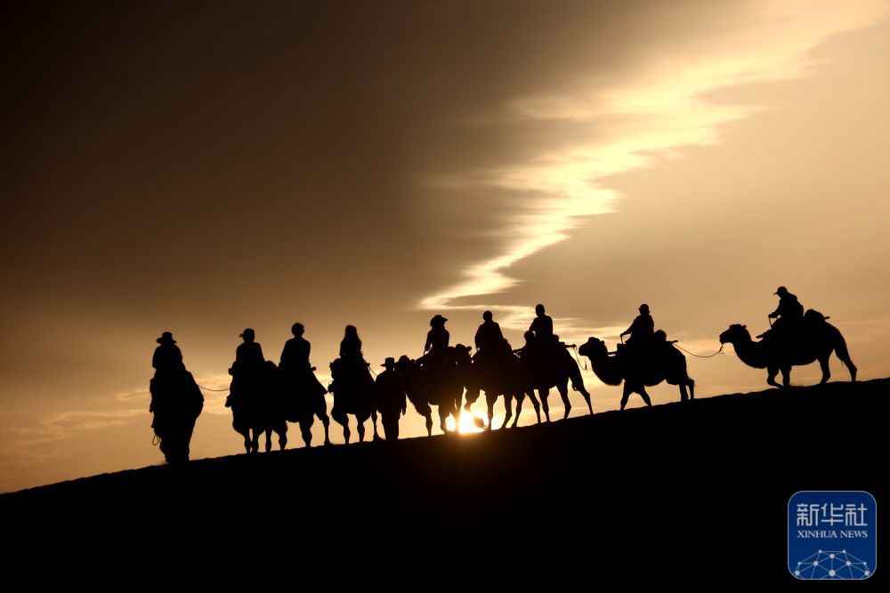 ↑9月1日清晨，游客在甘肃省敦煌市鸣沙山月牙泉景区乘骑骆驼，欣赏大漠风光，体验丝路风情。