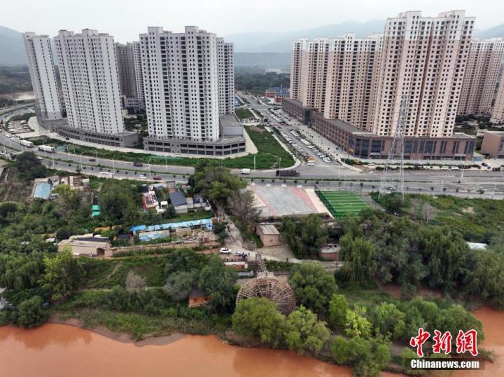 9月11日，无人机航拍甘肃省兰州市西固区新城镇三百多年的大水车与岸边的新建住宅楼。中新社记者　毛建军　摄