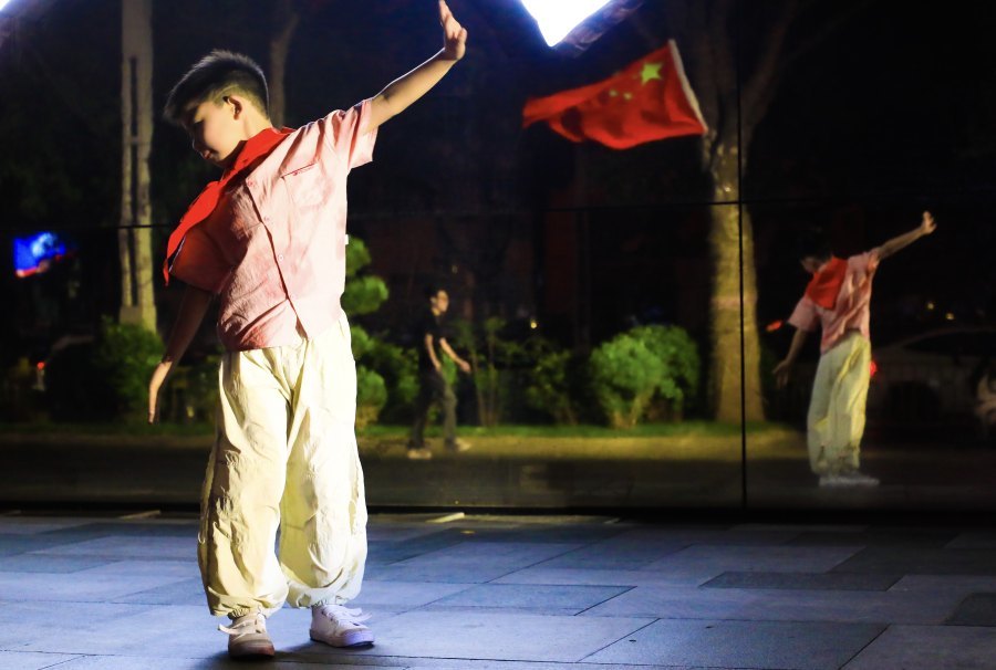 一位小朋友在万象城商场，旁边的五星红旗迎风而舞。