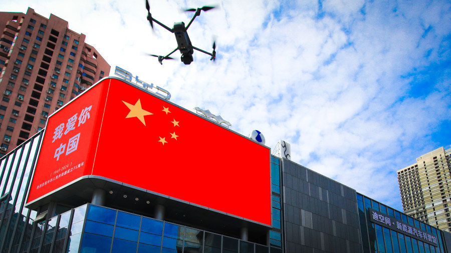 比亚迪•迪空间新能源汽车科普馆亮起了巨幅国旗图案，一架无人机正在拍摄。